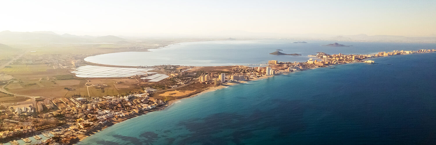 Aerial picturesque panoramic horizontal image, drone point of view La Manga del Mar Menor townscape and seaside spit of turqiouse Mediterranean Sea. Murcia, Spain. Travel and holidays concept